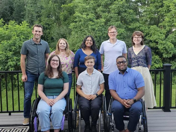 Group shot of people of various races and sexes, standing or seated on an outdoor deck