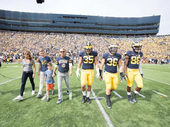 Nathan and Catherine Forbes were honorary captains during a 2015 Michigan Football game and are pictured on the field at Michigan Stadium with several players.