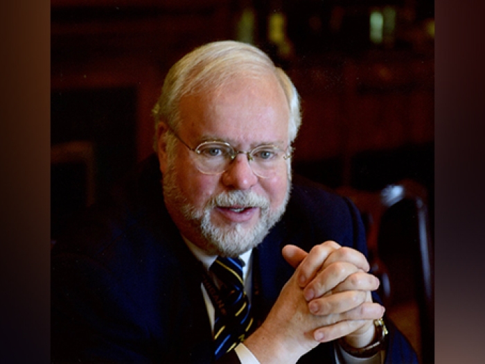Portrait of Tim Johnson, M.D. His hands are folded in front of him, and he is wearing glasses and a dark suit and tie.