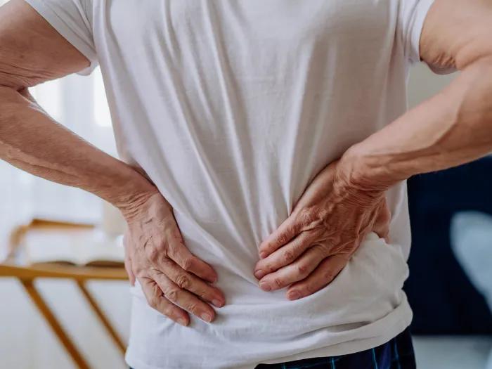 Main in a white t-shirt holding his lower back in pain
