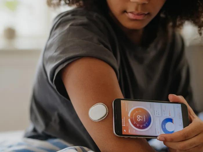teen girl in t-shirt checking device on arm linked to phone which she holds up to her arm 