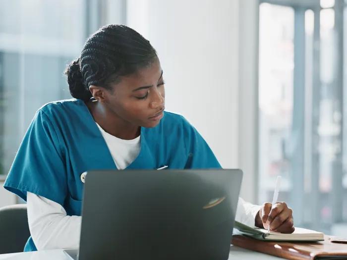 Photo of a woman sitting in front of a laptop taking notes