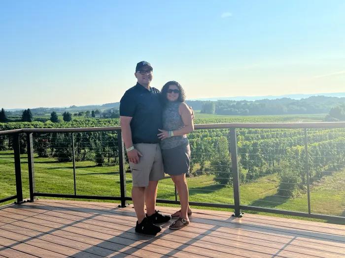 couple standing in front of a vineyard greenery on a deck sunny