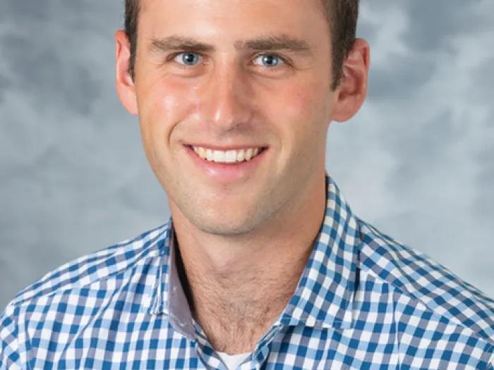 White man with dark brown hair in a blue and white checked shirt.