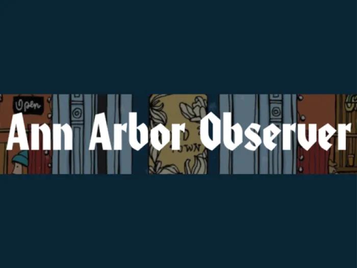 White text reading "Ann Arbor Observer" in a bold, stylized font is centered over a dark blue background. Behind the text there is a thin horizontal strip with illustrated elements including doors, windows, signage, and decorative patterns, evoking a local or urban scene.