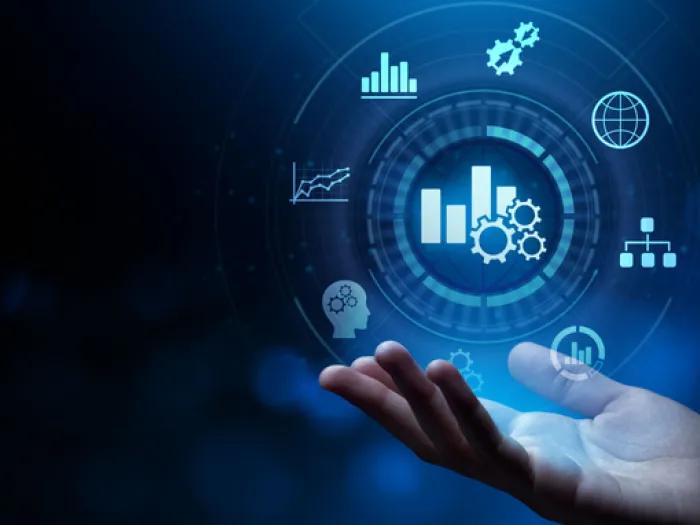 A person’s hand is extended upward with digital business and analytics icons floating above it, including graphs, gears, a globe, and a head with gears, all set against a dark blue, futuristic background.