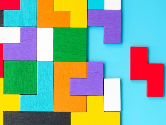 Colorful, wooden Tetris-style blocks arranged in a partially completed puzzle on a blue background, with one bright red piece set aside from the rest.
