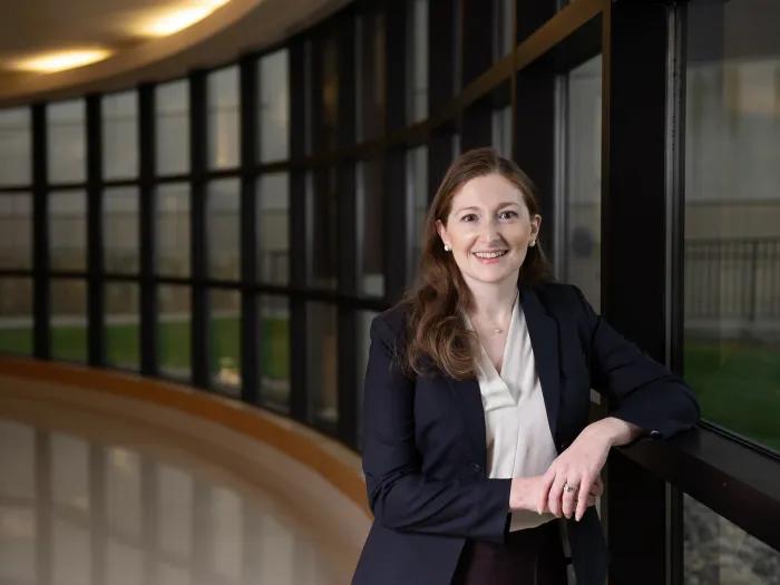 Smiling white woman with long dark red hair and a dark suit.