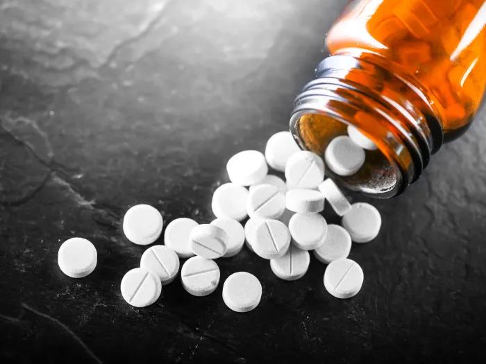 An orangish pill bottle with white round pills spilling out of it