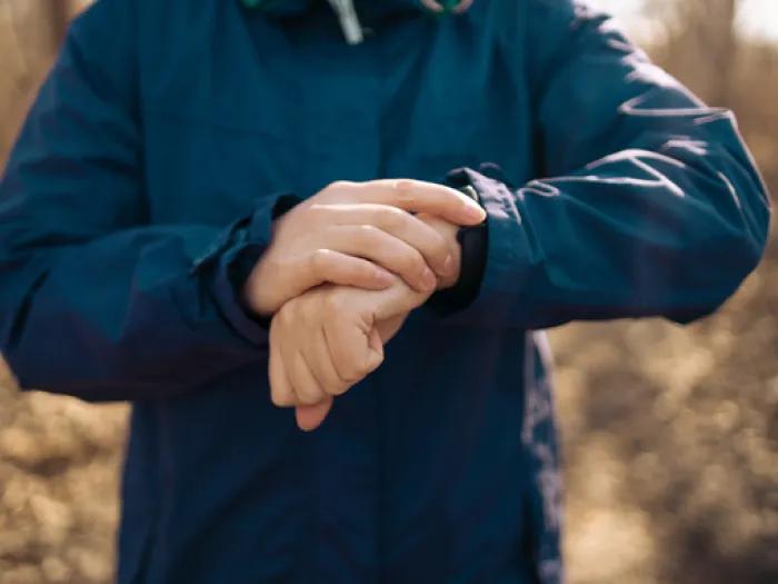 A person wearing a dark blue jacket touching a smartwatch on their left wrist outdoors, with a blurred natural background.
