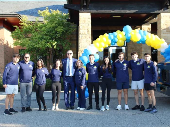 Members of the Shenandoah Young Adult Committee and others stand in front of a yellow and blue balloon arch in front of the Shenandoah Country Club.
