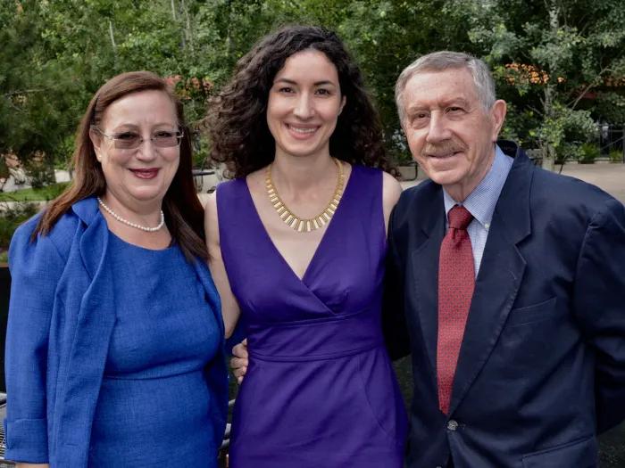From left to right, Giuseppina, Giulia, and Robert Ippolito smiling and standing together. They appear to be dressed for a special event. They are outside and there are trees and paved areas behind them.