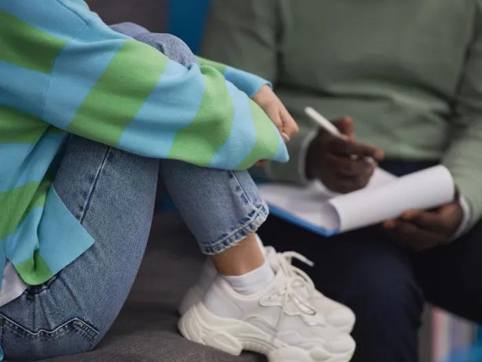 kids hugging legs with jeans on green light blue striped shirt white sneakers next to person with green shirt writing on white notepad