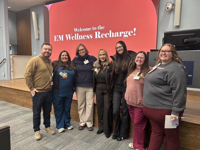Ground of people stand in front of a screen that reads "EM Wellness Recharge"
