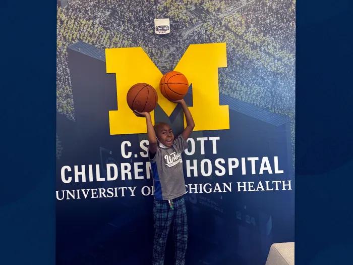 little boy with basketballs and Michigan C.S. Mott logo behind him