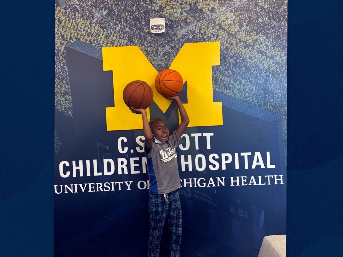 little boy with basketballs and Michigan C.S. Mott logo behind him