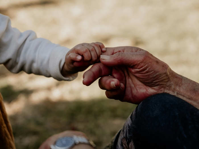 A child's hand holding on to an elderly person's index finger. (Photo by Loume Visser on Unsplash)