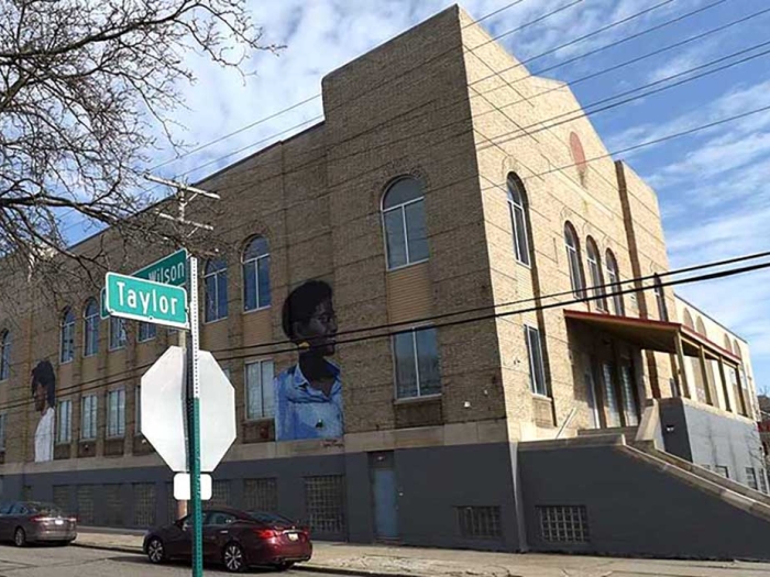 View of a cream colored two story building with a mural of a young black girl