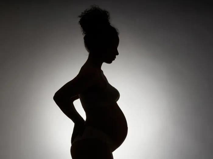 silhouette of pregnant woman black on grey background with white background behind the body glowing