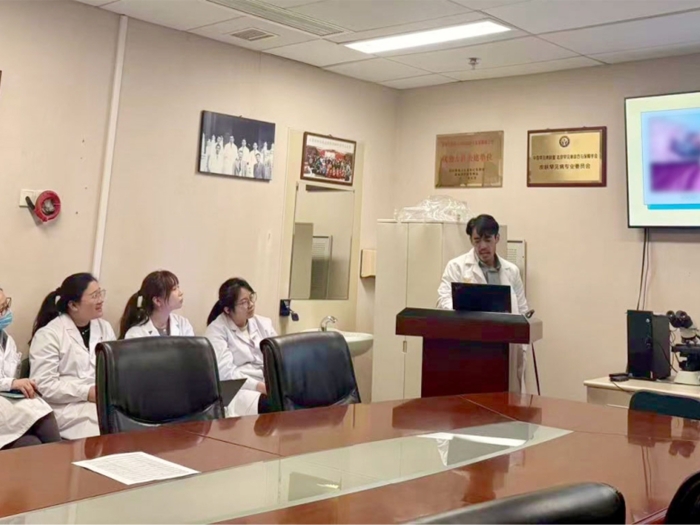 doctor presenting in conference room to other doctors in white coats table in middle and screen 