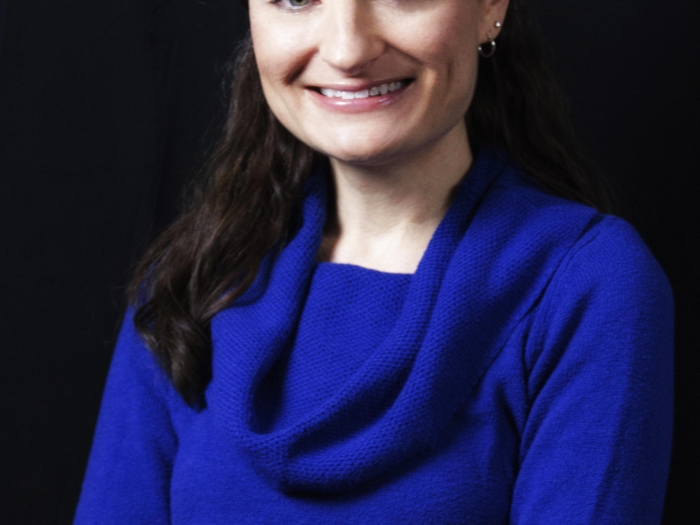 Women with black hair and a blue shirt, set against a black background.