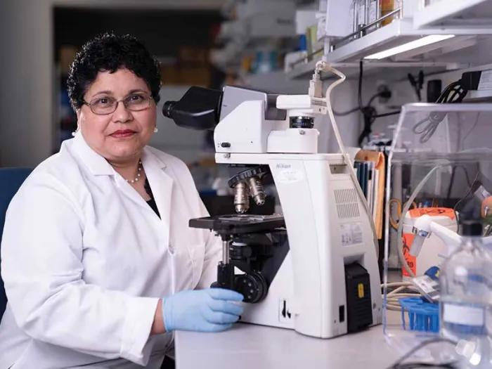 Nisha D'Silva, BDS, MSD, PhD sits next to a microscope
