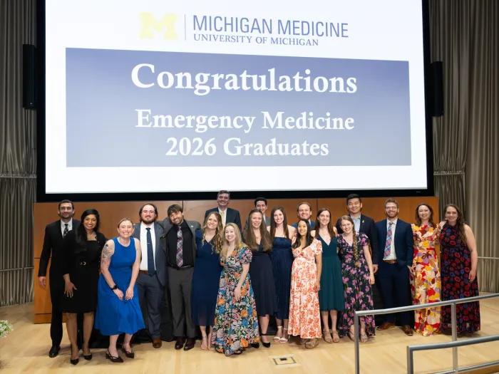 Graduating Residents and fellows pose for a photo in from of a screen that says "Congratulations Emergency medicine 2026 graduates"