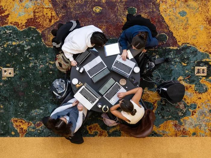 four people sitting at a table with laptops collaborating