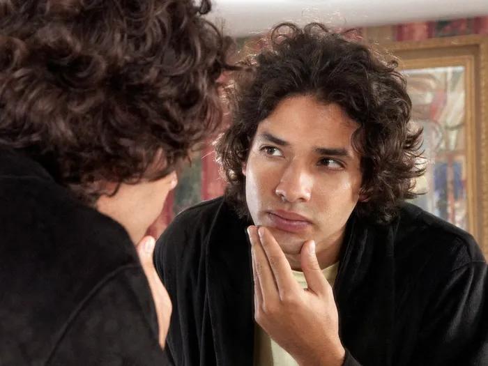 man looking in mirror curious at face