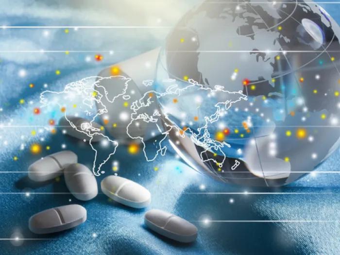 Prescription pills beside a globe overlaid with a world map and glowing connection points, representing global medication and treatment patterns