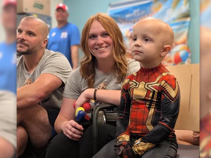 boy dressed as spiderman next to woman red hair smiling and man sitting on floor in playroom