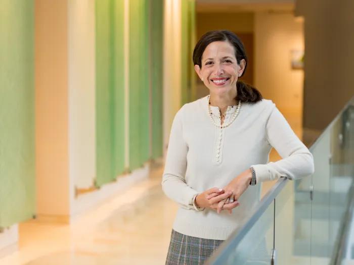 Dr. Jacqueline Jeruss leaning against a glass rail wearing a white sweater.