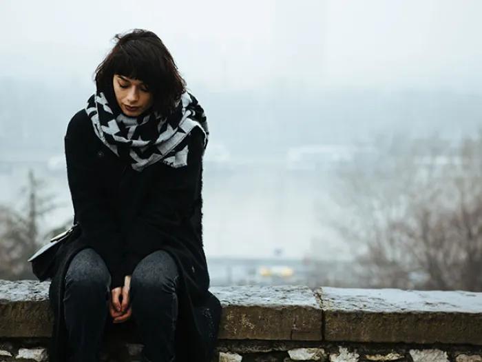 young woman lookin down at the ground wearing black on a foggy day