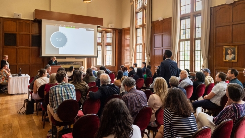 A group of attendees sitting in a large, elegant room listening to a presentation, with a projected slide that reads 'Thank You!' on display.