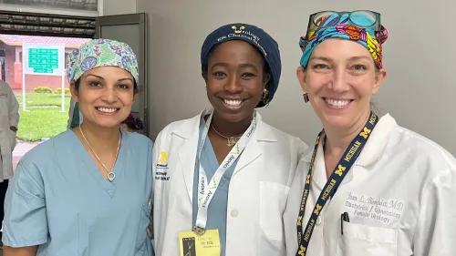Three clinicians—two in white coats, one in scrubs—smile together in a clinic hallway during a urology partnership visit