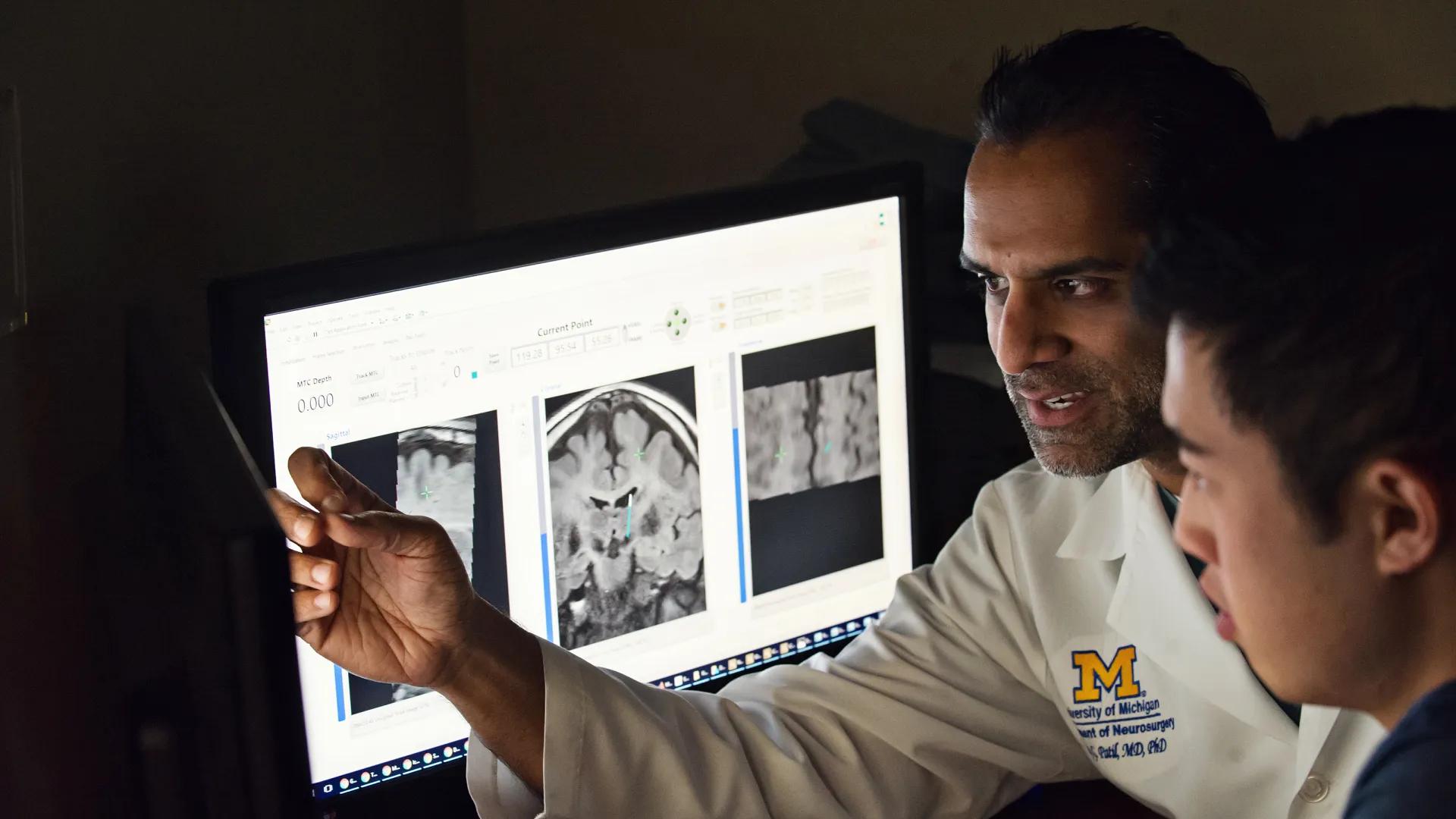 Two men looking at computer screen with brain images, one pointing