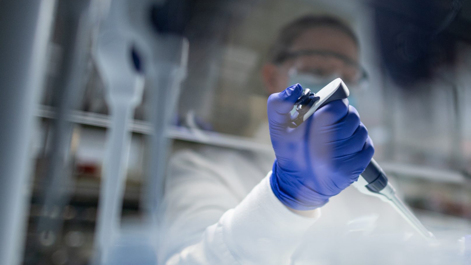 faded image of researcher in lab using pipette