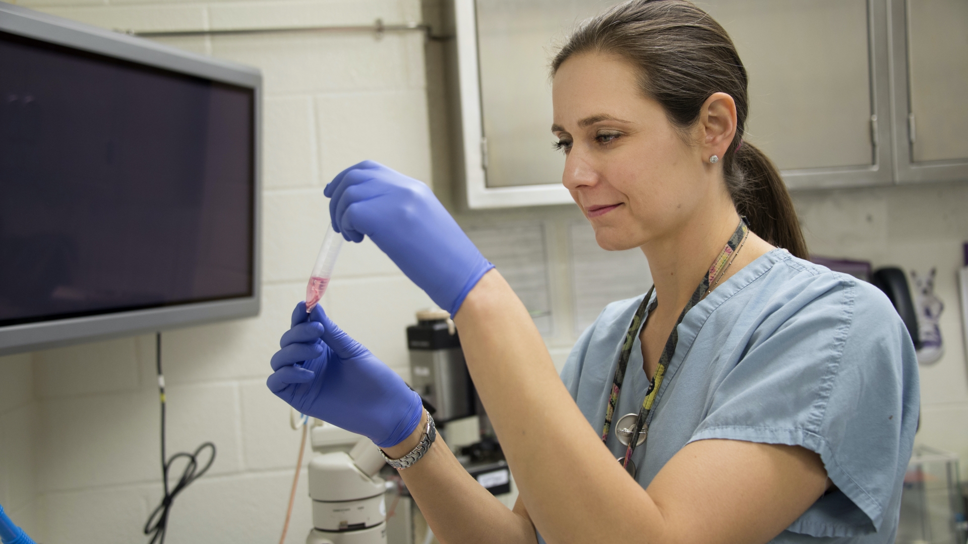 Woman with gloves and medical clothing holding a test tube 