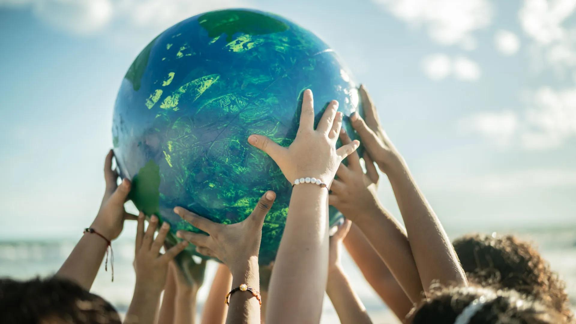 Four people hold a beach ball sized globe over their heads