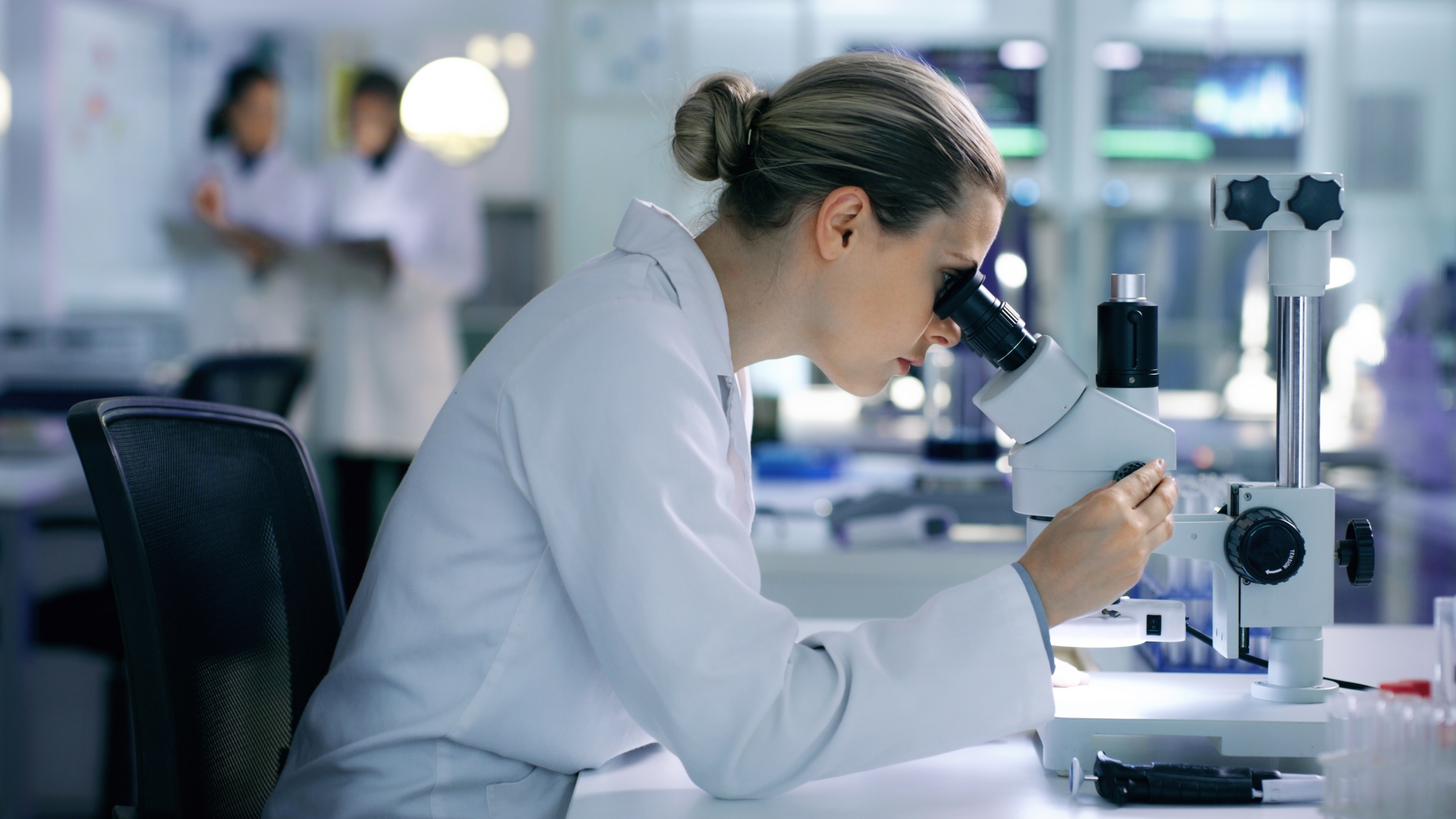 Female scientist looking into a microscope with two researchers in the background