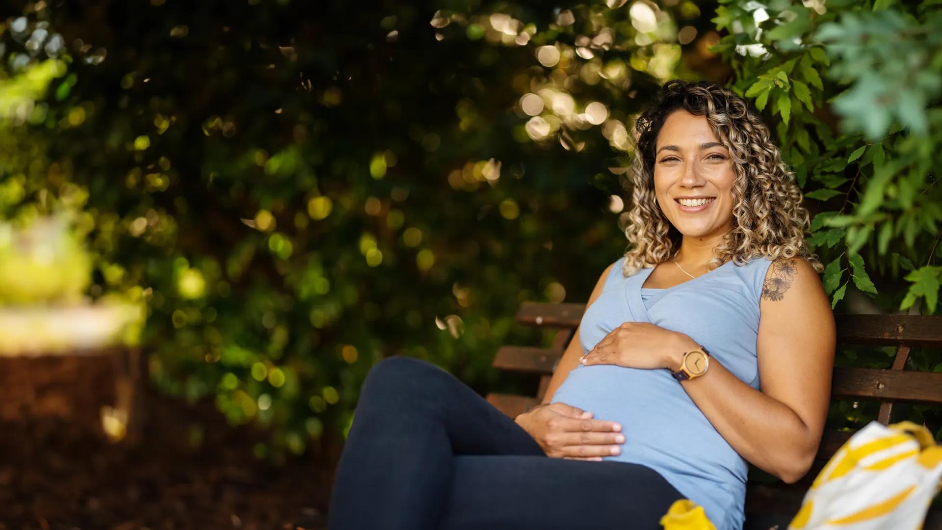 pregnant woman smiling sitting on a bench outside