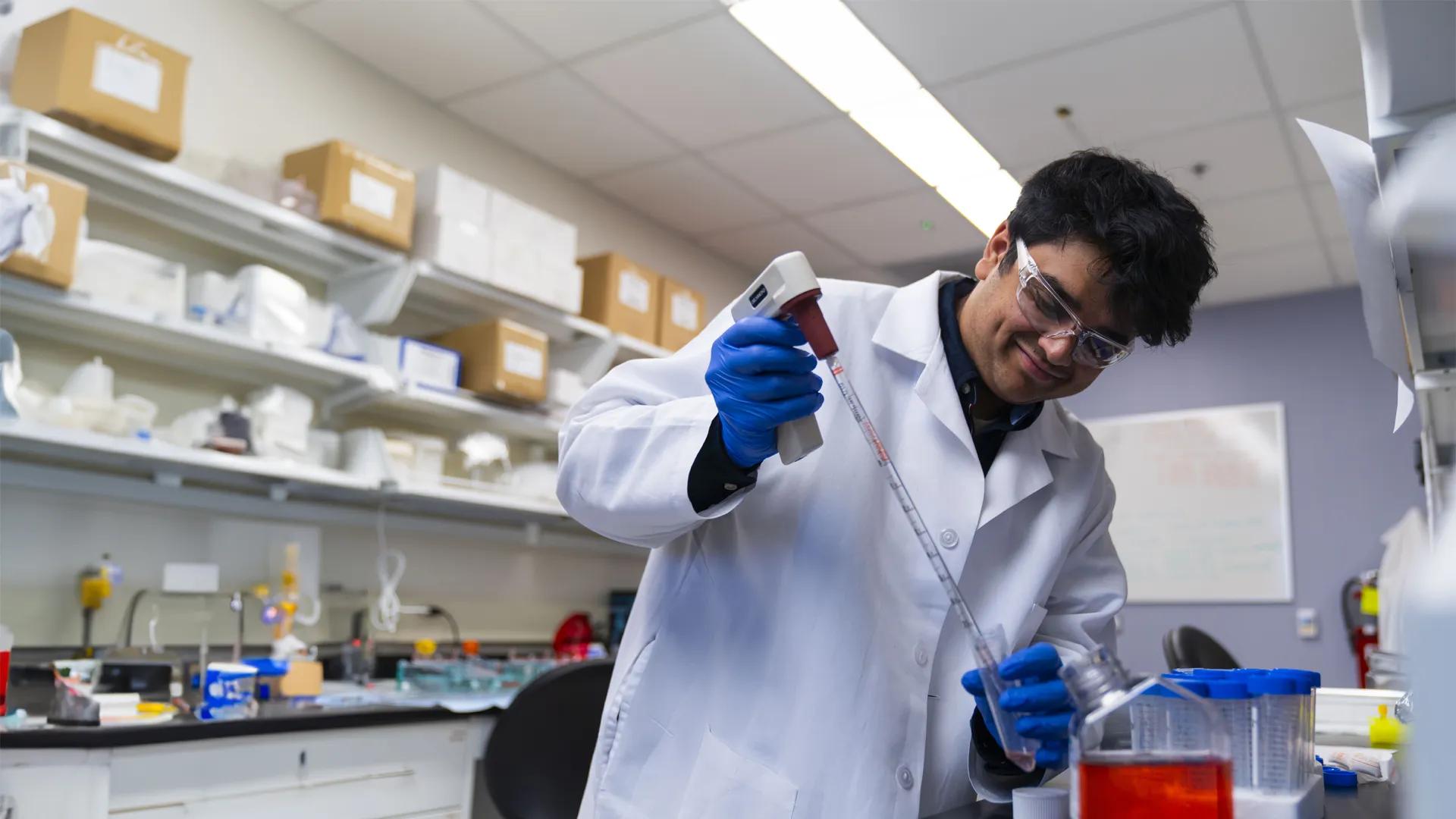 young researcher smiling in a lab holding a pipette