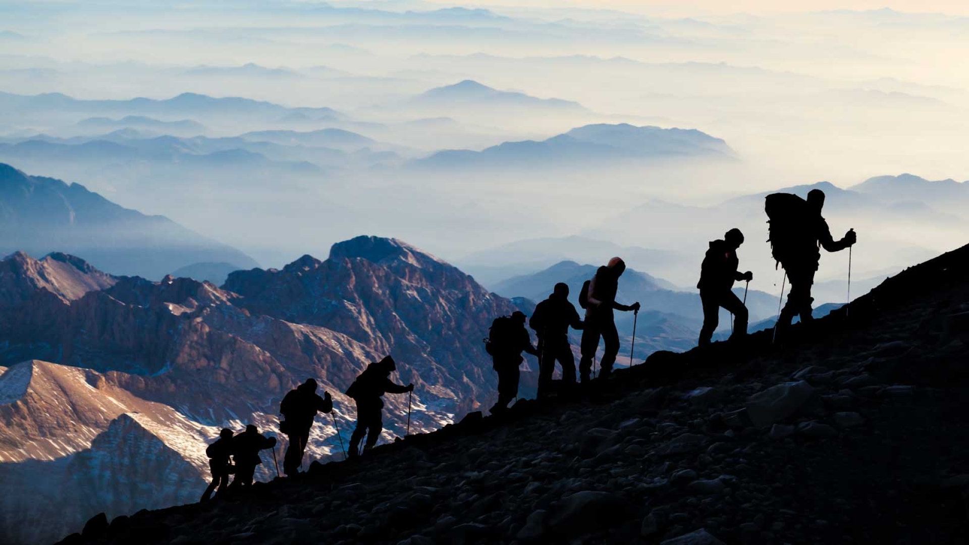 Nine hikers in silhouette climbing a mountain with a scenic mountain view behind