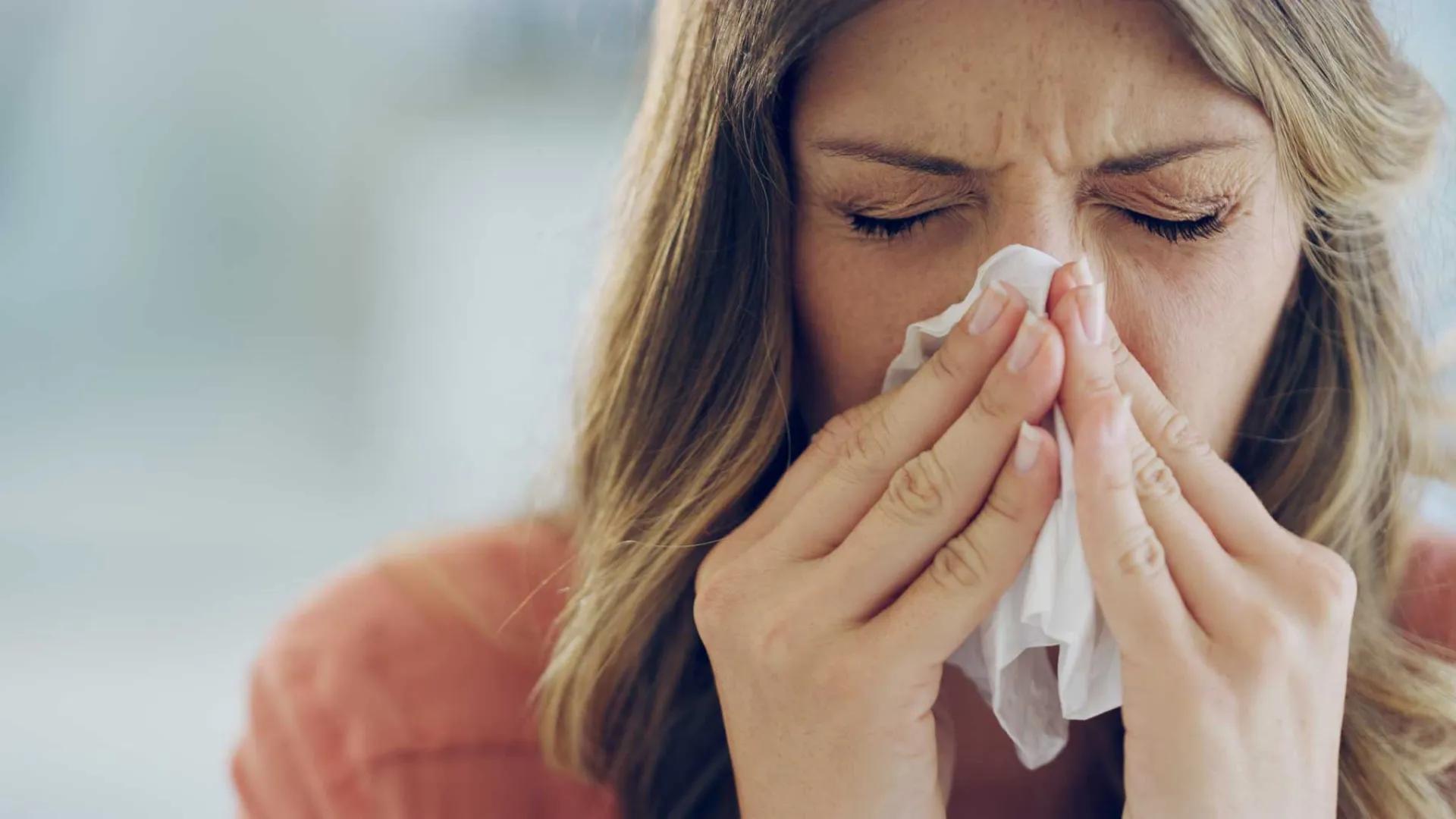 A woman with sinus pain wiping her nose with a kleenex using both hands