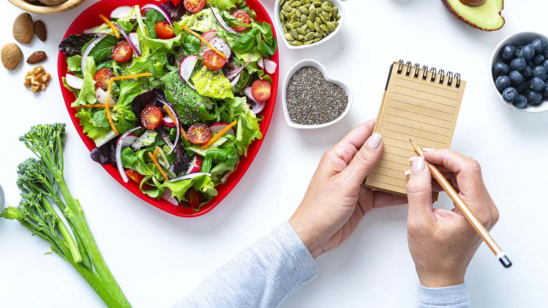 close-up of person writing notes near plates of vegetables