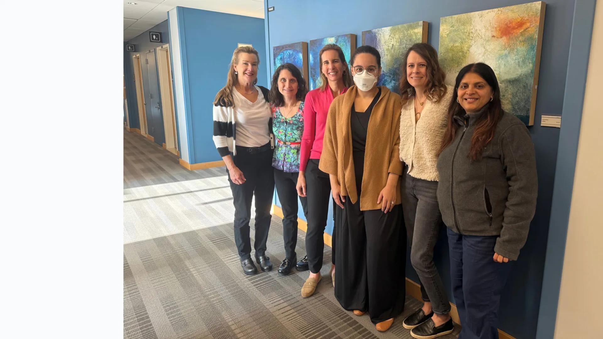 Six members of the Woodward Lab team standing against a blue wall with watercolor paintings