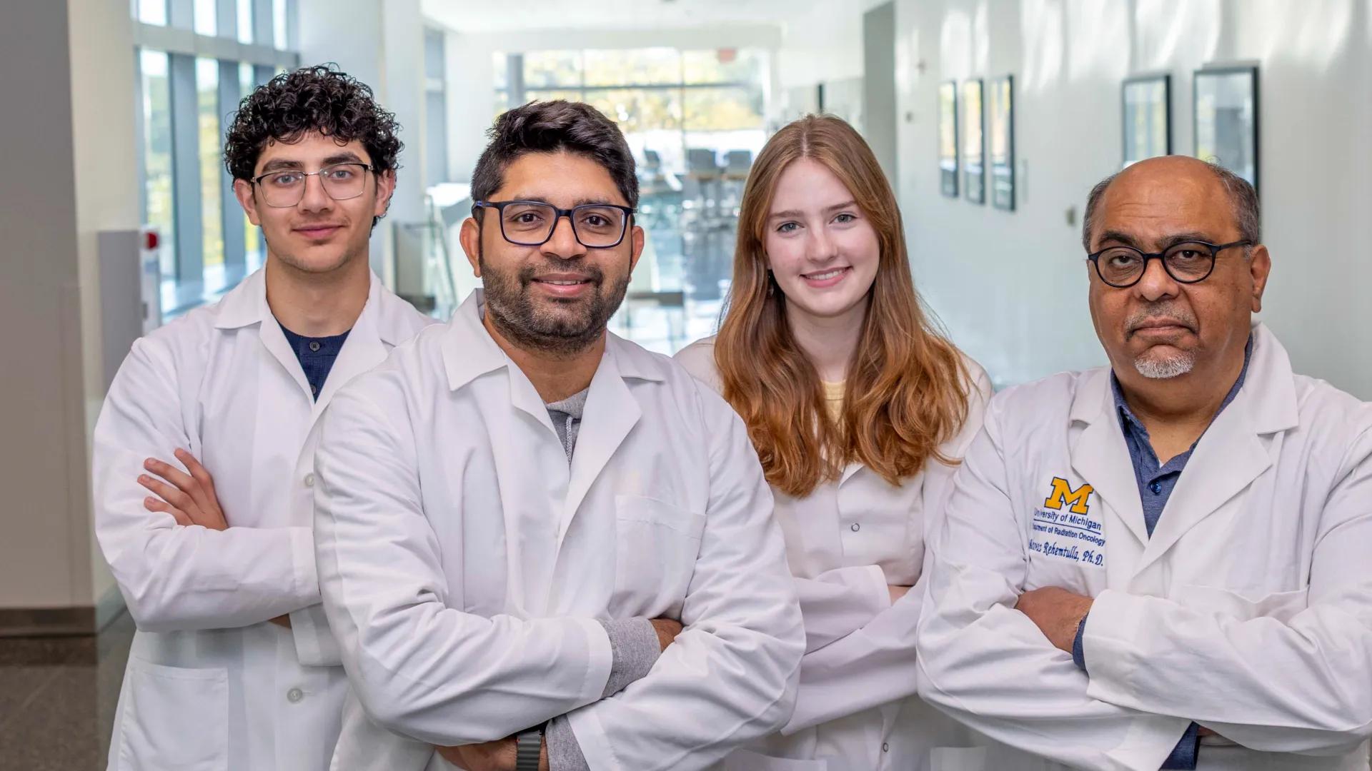 Four people in lab coats stand confidently in a bright hallway, smiling. 