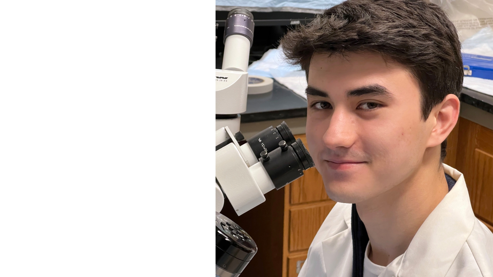 Person sitting at a microscope looking at the camera.