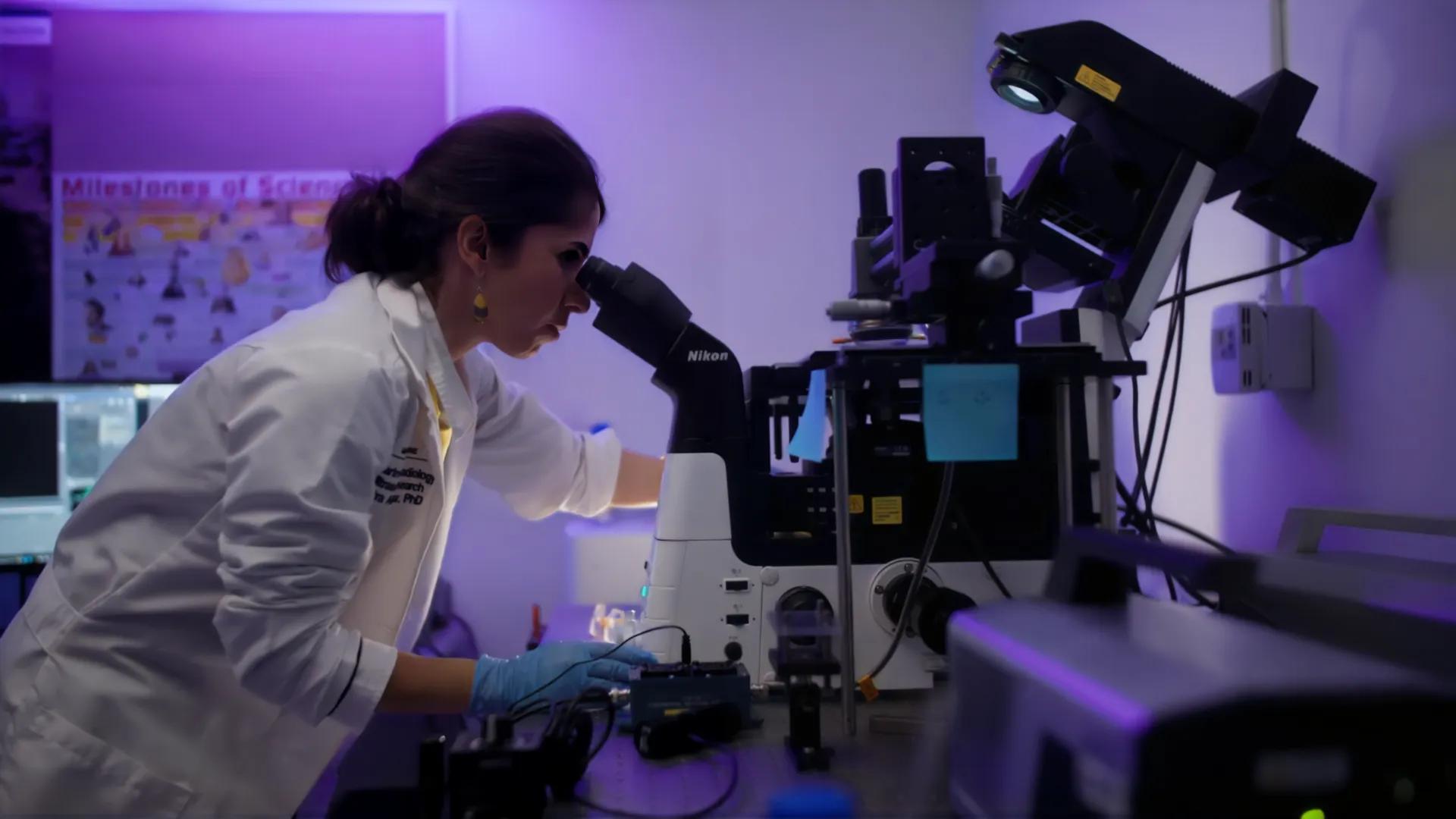 Photo of a woman looking into a microscope in a lab