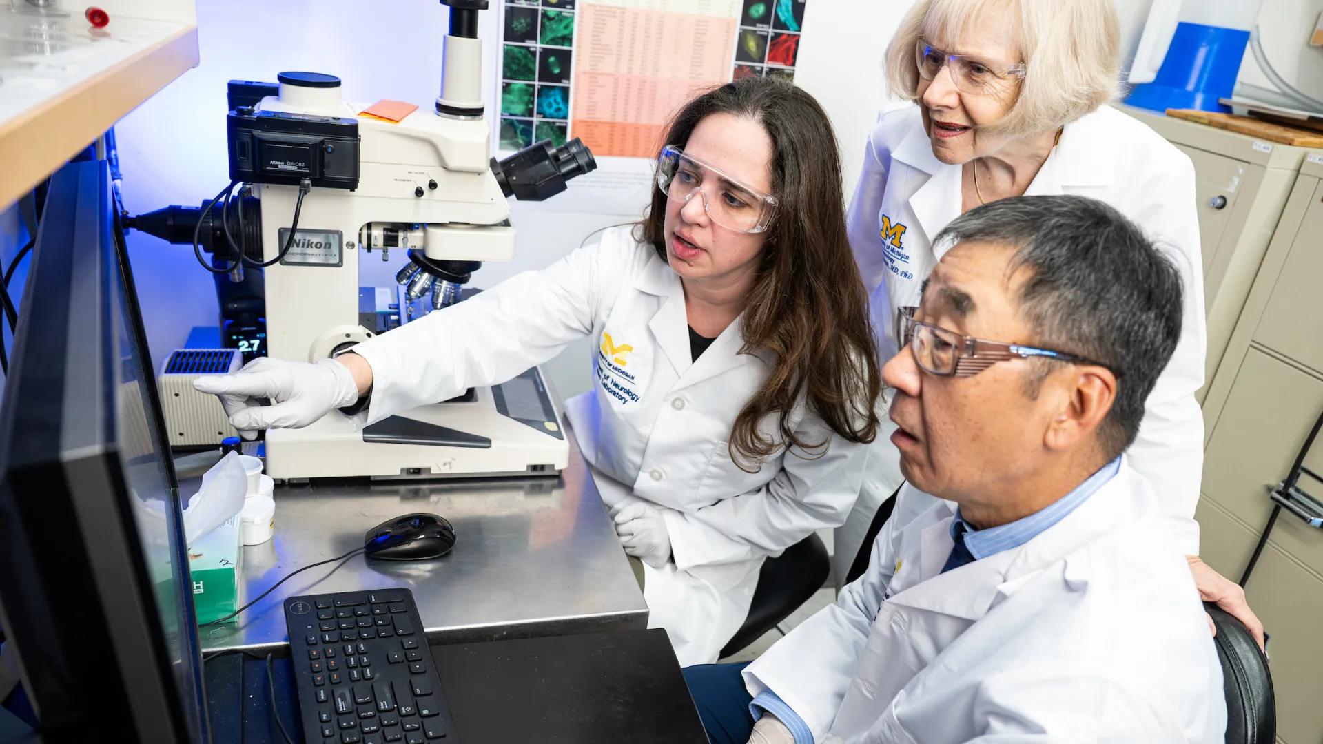 Drs. Laura DeVault, Eva Feldman and Bhumsoo Kim in lab coats in the lab looking at a monitor